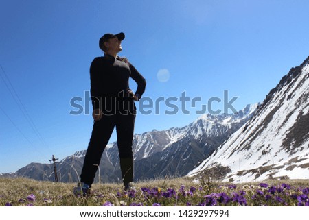 Lonely standing girl in a cap on a flower meadow, looking into the distance, against the background of snow-capped mountains