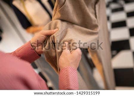 Checking the textile. Close-up picture of man checking the textile of beige pants while being in the showroom.