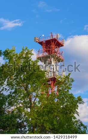 metal tower with cellular repeaters installed on it for signal transmission, against the background of trees, sky and clouds