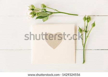 Pink roses with craft paper envelope with heart.Minimalist flat lay,white wooden background.Mock up for design.