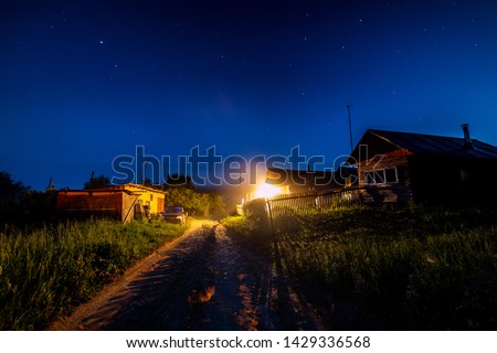 Starry night sky over village house in summer. Wooden house with one bulb light over entrance. Russia.