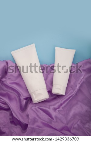 White tube cosmetics cream on violet textile background. Flat lay