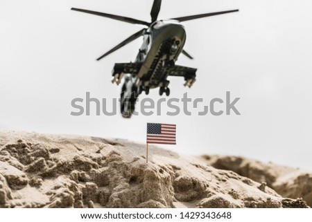 selective focus of small american flag on sand dune with military helicopter above