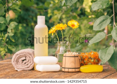 Spa products and accessories. Towel, soap and plastic bottle with marigold extract, calendula flowers in a glass flask and wooden bowl with dry flowers of chamomile on wooden boards.