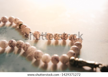 Conceptual close up shot of prayer beads and bright sun flare from the back in the evening with copy space. Selective focus with shallow depth of field. Image may contain soft focus and noise texture.