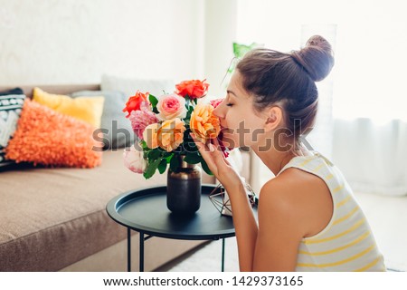 Woman smelling fresh roses in vase on table. Housewife taking care of coziness in apartment. Interior and decor Royalty-Free Stock Photo #1429373165