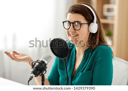 technology, mass media and people concept - woman in glasses with microphone and headphones talking and recording podcast at studio