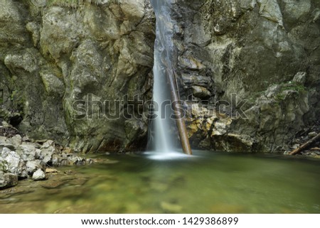 Close up of a tall waterfall in the Alps, flowing into a clear green mountain lake. Background textured rocks. Foreground clear green water. Due to long exposure, the water seems soft and fluffy.