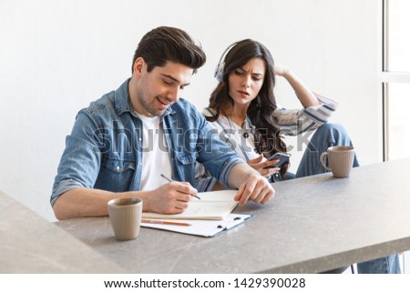 Attractive young couple drinking coffee in the morning at home, sitting at the table, studying, listening to music with headphones