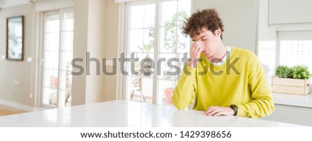 Wide angle shot of young handsome man at home tired rubbing nose and eyes feeling fatigue and headache. Stress and frustration concept.