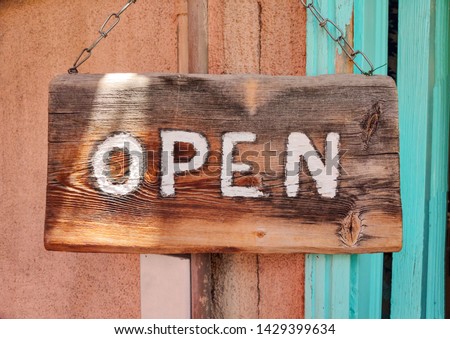 Open text on wooden sign board hanged with a metal chain on a buildings facade, close up view