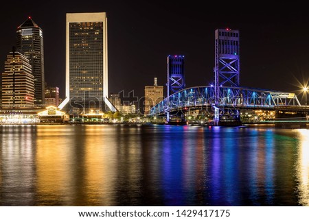 Jacksonville at night with buildings and a bridge reflecting on the river.