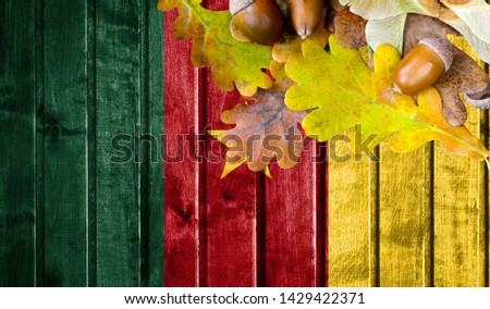 Cameroon flag on autumn wooden background with leaves and good place for your text.
