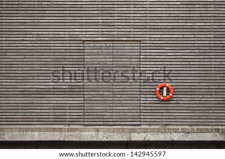 Red lifebuoy and closed door on weathered wooden wall in port