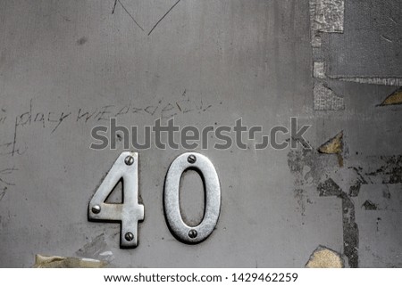 House number 40 with the forty in silver metal digits on a gray dirty and beaten up front door - banged up, used and abused