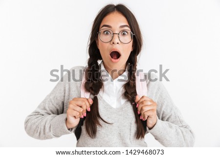 Photo closeup of shocked teenage girl wearing eyeglasses carrying backpack and wondering at camera with open mouth isolated over white background