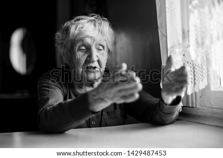 The old lady is sitting talking gesticulating at the kitchen table. Black and white photo.