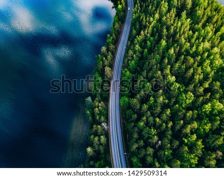 Aerial view of road between green summer forest and blue lake in Finland Royalty-Free Stock Photo #1429509314
