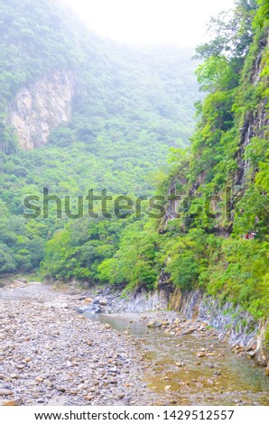 Vertical picture of Taroko National Park in Taiwan. Named after beautiful Taroko Gorge, popular tourist attraction. River surrounded by tropical forests and steep rocks. Misty, foggy weather. Rain.