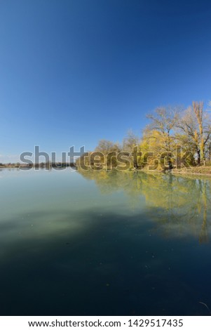 Panorama of the evening lake with blue water and trees with yellow leaves on the shore against the blue sky in the foothills of the North Caucasus                               