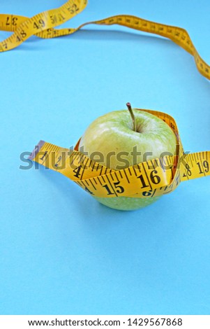 a fresh crisp green apple on a einfabrigen surface and are wrapped by a measuring tape - concept for healthy weight loss that makes fun