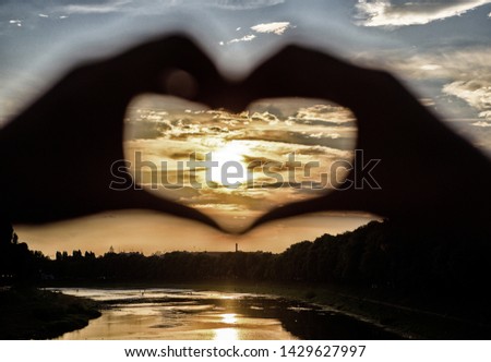 Heart gesture in front of sunset above river. Romantic date ideas. Idea honeymoon travel. Vacation resort. Sunset sunlight romantic atmosphere. Hands in heart shape gesture symbol of love and romance.