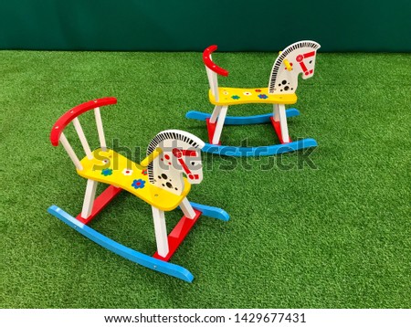 Two colorful wooden rocking horses on artificial grass in the playground.