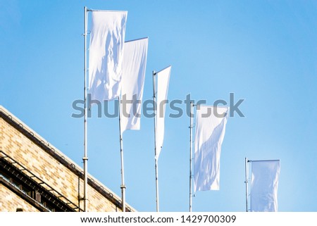Three blank white flags on flagpoles against cloudy blue sky with perspective, corporate flag mockup to ad logo, text or symbol, company identity flag template with copy space