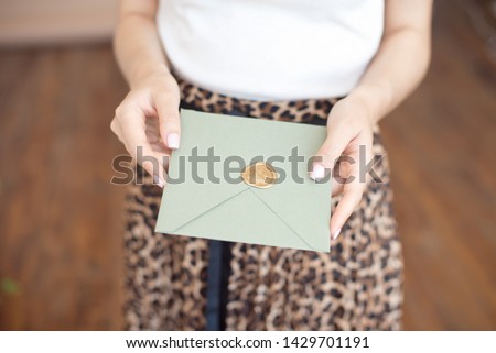 Close-up photo of female hands holding a silver blue or pink invitation envelope with a wax seal, a gift certificate, a postcard, a wedding invitation card