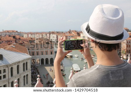 young boy with hat takes picutres with smartphone Grand Canal and old Palaces in Venice Italy