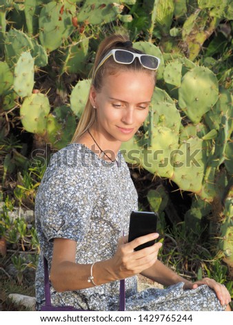 Pretty woman wearing a dress taking a picture of a cactus cell phone.