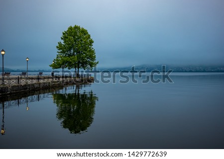 Ioannina, Greece, lake misty early spring morning with fog over the lake Pamvotida calm waters. Tree reflection, high contrast mystical picture
