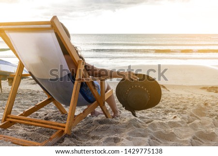 Woman sitting in a beach chair holding her hat watching a beautiful sunset on the beach. Royalty-Free Stock Photo #1429775138