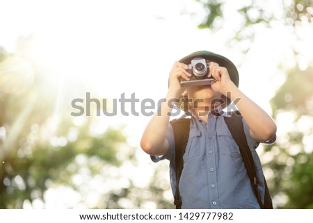 Portrait of little explorer with photo camera in forest. Boy traveler in helmet play in the park. Happy child go hiking with backpack in summer nature.