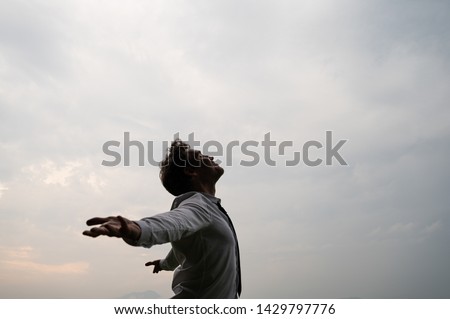 Peaceful young businessman standing with his arms spread looking up towards a cloudy sky. Royalty-Free Stock Photo #1429797776