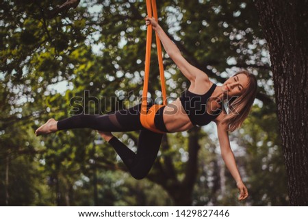 Beautiful pensive girl with long hair is doing exercises on sling in the summer forest.