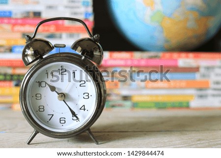 Close-up of an ancient alarm clock on the floor Many colorful books in the background selective focus and shallow depth of field