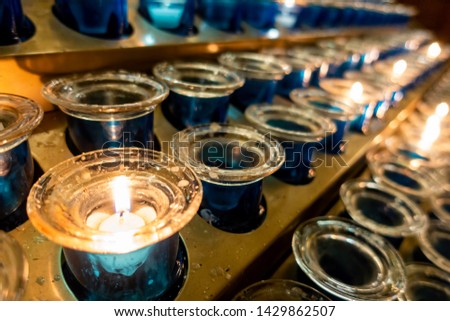 A series of devotional tea light candles arranged on a stand. Low-light image. Commonly seen inside churches.