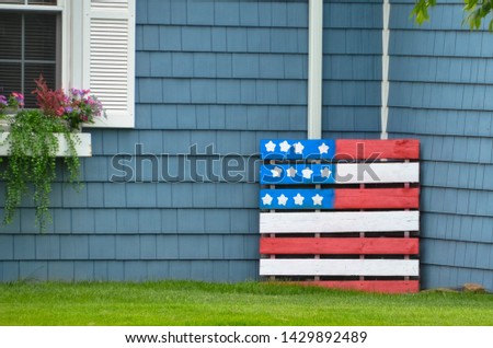 pallet american flag decoration against blue exterior of home white shutters on a window with flower box patriotic holiday decoration