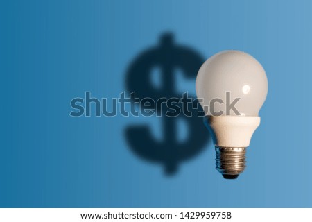 Light bulb on bright blue background with a dollar sign shadow. Conception good idea it's money.