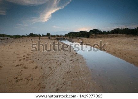 view of beautiful beach with small river at fishing village during sunset