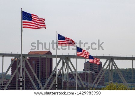 Four flags swaying on the sky with Cincinnati bridges and downtown building on the background.