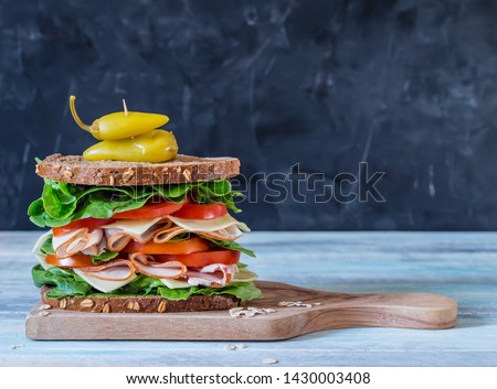 Ultimate deli or club sandwich with turkey pastrami lettuce and tomatoes on grey background with copy space