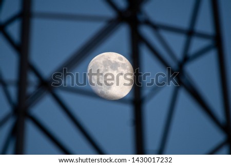 Moon captured with long lens with metal structure from electrical supply poles in foreground.