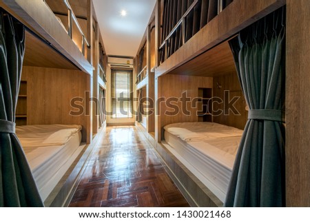 Hostel dormitory beds arranged in dorm room with white plain bunk bed in dormitory.Hotel dormitory have many beds arranged in one room. Clean hostel small room with wooden bunk beds.  Royalty-Free Stock Photo #1430021468