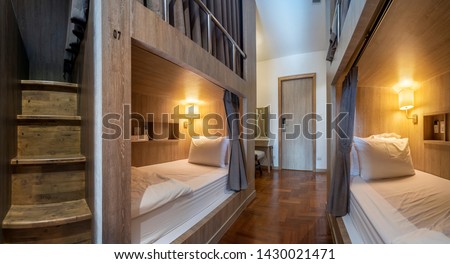 Hostel dormitory beds arranged in dorm room with white plain bunk bed in dormitory.Hostel dormitory have many beds arranged in one room. Clean hostel small room with wooden bunk beds. small hotel  Royalty-Free Stock Photo #1430021471