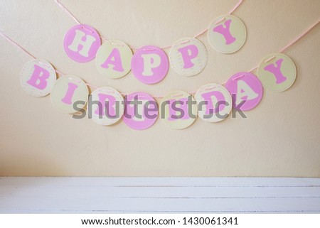 Circle “happy birthday” flag with pink ribbon decoration on concrete wall background and white wooden floor.