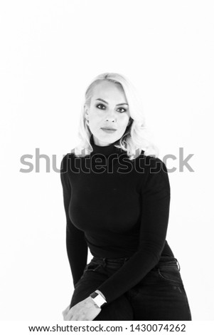 Black and white studio portrait of an attractive blond woman in a black turtleneck jumper against plain background