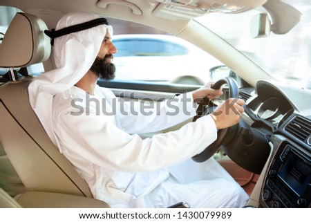 Successful arab saudi businessman riding his car or driving full of emotions at sunny day. Male model as an enterpreneur. Concept of business, finance, modern technologies, start up, economy.