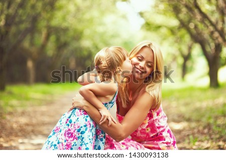 Little blonde girl kissing her blonde mother in the park